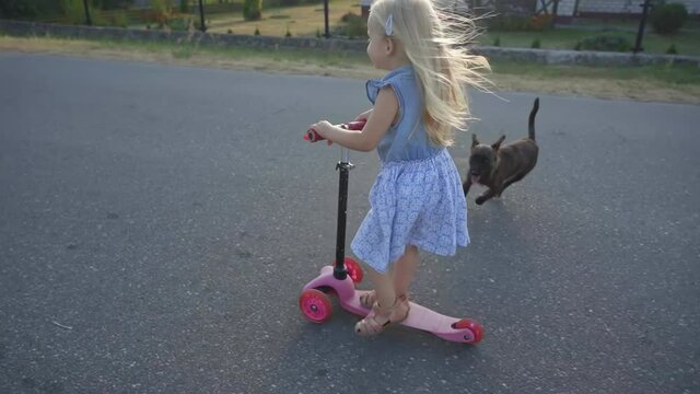 A little girl in the village rides a scooter.