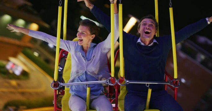 Top view shot of a happy smiling father and little daughter are having fun to drive a bumper car together at fun fair in amusement park with luna park lights at night.