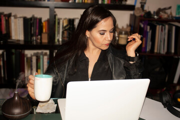 .Woman in office reviewing documents and reports on laptop while enjoying coffee and steam from humidifier