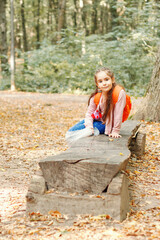 Walking girl in a pink jacket with an orange backpack in the autumn forest during leaf fall