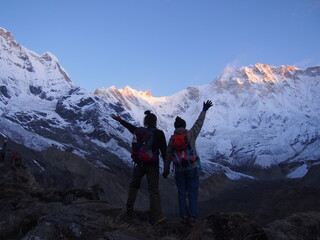 Mountain climbers raise their arms in front of a snow-covered Himalayas in the morning sun, ABC (Annapurna Base Camp) Trek, Annapurna, Nepal