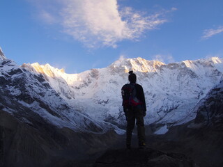 A mountain climber standing on a rock near the top and watches the sunrise over a snow-covered...