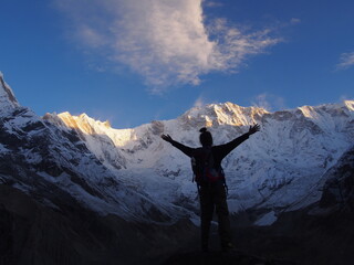 A mountain climber raises his arms in front of a snow-covered Himalayas in the morning sun, ABC (Annapurna Base Camp) Trek, Annapurna, Nepal