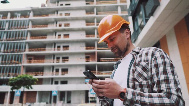 Young Engineer using smartphone on construction site. Architect using phone. Manager development building texting on smart phone. Builder makes notes in application during inspection and verification