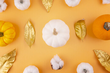 White and orange heirloom pumpkins, cotton flower, autumn golden leaves on orange backdrop. Halloween background flat lay. Thanksgiving holiday decor