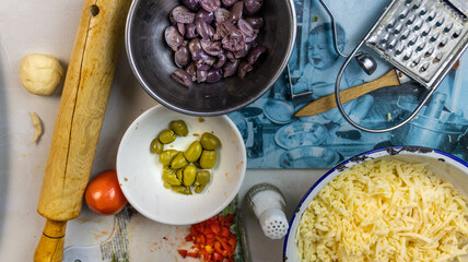 Bowl of black and green olives, chopped bell pepper, grated cheese, brush, grater, kitchen chopper, eaves on a kitchen set

