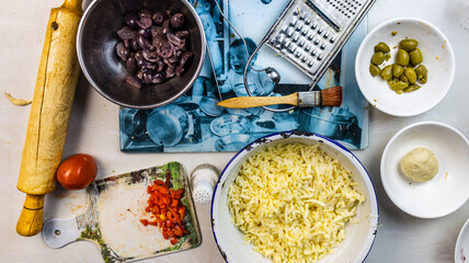 Bowl of black and green olives, chopped bell pepper, grated cheese, brush, grater, kitchen chopper, eaves on a kitchen set
