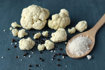 Fresh vegetarian products for dinner preparation. Cauliflower with pepper and salt on a wooden spoon on a dark background. A simple recipe of vegetables. Diet. Selective focus