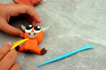 The girl is holding a figurine in the form of a bull made of airy plasticine, children's creativity, with her own hands, a symbol of the year 2021.
