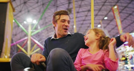 Authentic shot of a happy smiling family is having fun to drive and crush bumper cars at fun fair in amusement park with luna park lights at night. - Powered by Adobe