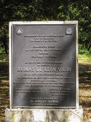 Leon, Nicaragua - November 27, 2008: Closeup of Black metal official plate at entrance to Ruinas de Leon Viejo museum park. Green foliage in back.