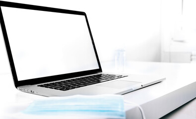 Modern laptop with a medical face mask on top of a white desk.