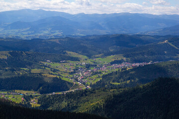 Obraz premium Village in mountain, backdrop with high dark green peaks, blue sky with a lot of white clouds