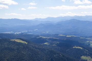 Obraz premium Summer mountains with dark green grass and trees. Blue sky with white clouds, landscape backdrop with mountains high peaks