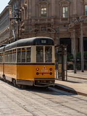 A yellow tram passes through the streets of the city of Milan