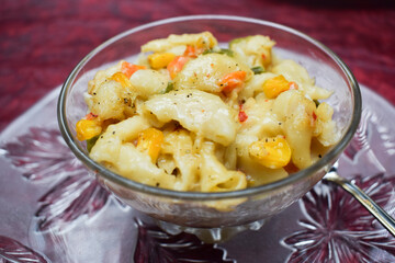 Close up of Vegetable macaroni cooked in White sauce served in a transparent bowl isolated on textured background. Cooked pasta with carrot, corn, capsicum sprinkled oregano and chillyflakes