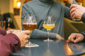 A group of friends at the bar drinking beer at a table. Close-up of male hands and glasses with alcohol