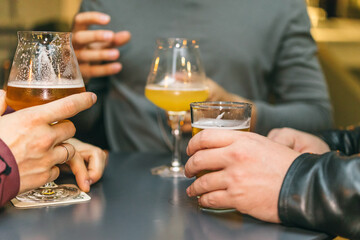 A group of friends at the bar drinking beer at a table. Close-up of male hands and glasses with alcohol