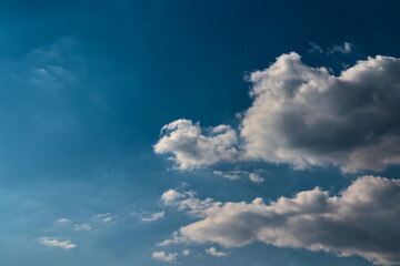 blue sky covered by a fine mist, with two light gray shaded cumulus clouds floating on the right side of the image.