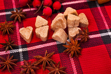 Christmas background. Star anise spices, hearts made of brown sugar and red hawthorn berries on a red fabric background. 