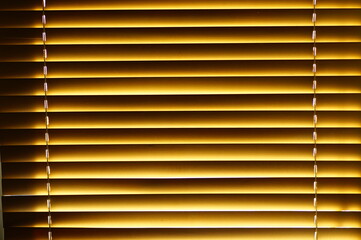 Abstract background - wooden blinds on the window, large brown-golden horizontal stripes lit by the sun