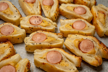 Baking Bun with Sausage and mustard puff pastry rolls. Delicious snacks, tapas, breakfast, appetizers on baking paper. Top view. Close-up