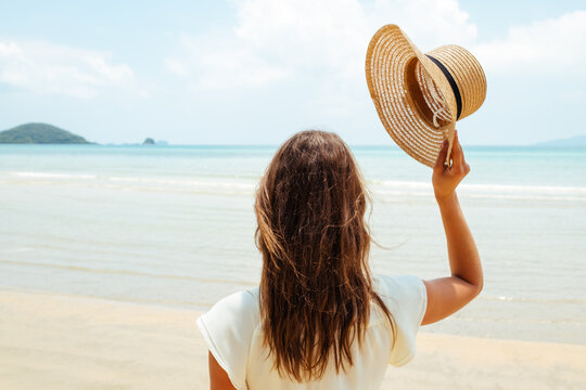 Beautiful young woman raises her hat on a beach
