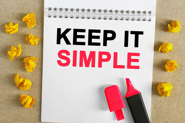 The text is written in the notebook - KEEP IT SIMPLE. There is a marker on the notebook, next to it is crumpled yellow paper.