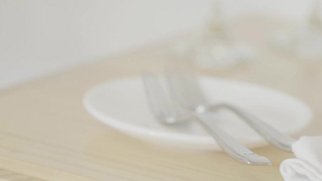 Close up of a white plate of dish with silver cutlery on top of it. The objects are on a light brown table.
