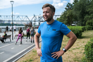 handsome male athlete in blue sportswear looks directly at the camera and smiles after an outdoor workout.