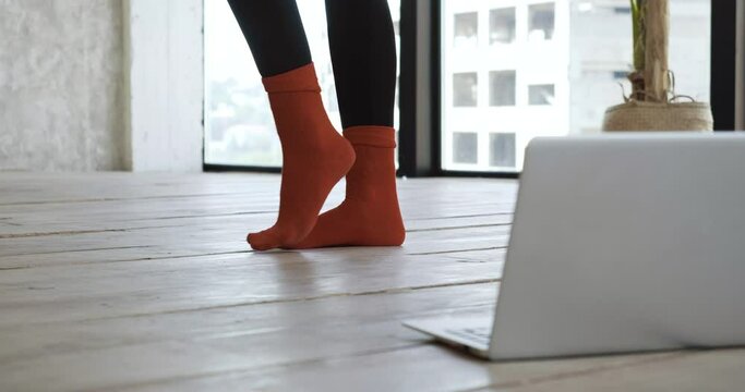 Close up of part of body female legs in warm red socks stand on floor in apartment home gym near laptop, goes in for sports exercises online remotely, stretches toes fingers before doing ballet dances