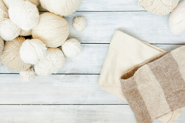 light wool yarn balls for knitting and knitted warm scarf on white wooden table, top view, selective focus