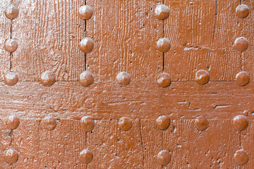 Old wooden wall with metal rivets painted orange.