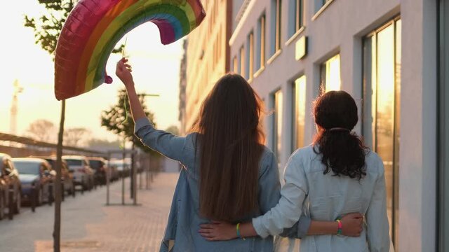 Two lesbian woman lgbt same-sex couple hugging with rainbow symbol balloon outdoors. Gay lesbians bisexual, transgender movements. Concept of LGBT happiness, freedom, love homosexual couple 4 K slowmo