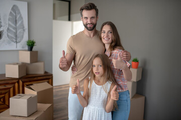 Young family standing together in the room and showing thumbs up