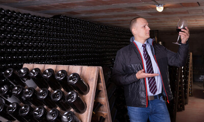 Professional sommelier tasting red wines in winery basement full of wine racks