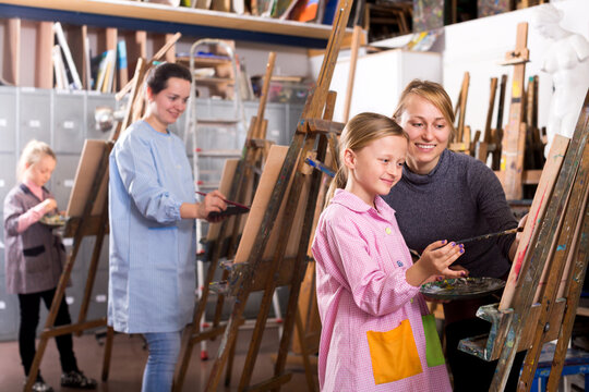Glad female teacher helping girl during painting class at art studio
