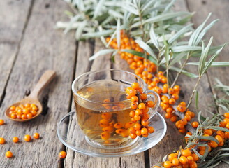Sea buckthorn branches with berries, tea, honey and sea buckthorn jam on a wooden background. The...
