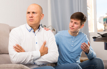 Obraz premium Teen boy trying to apologize his irritated father after dispute
