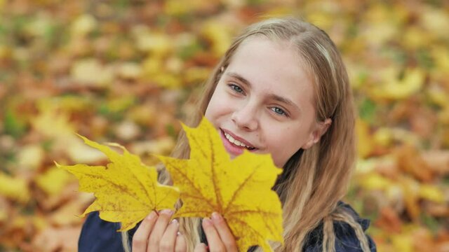 A young girl of 13 years old with autumn leaves poses in front of a video camera.