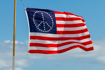 A stars and stripes United States flag with the stars oriented in the shape of the Peace sign. This flag is waving on a pole on a windy day promoting pacifist, anti war ideas
