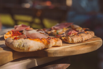 Two home made pizzas freshly baked and served on a wooden plate on a rustical table in a garden....