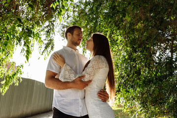 A man and a woman embrace under the branches of an old tree. People are illuminated by a contour light. A guy and a woman in white. High quality photo