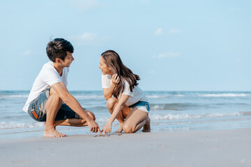 Fototapeta premium Romantic couple draw heart shapes in the sand on the beach.