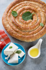 Greek spanakopita or spiral pie made of filo dough, spinach and feta cheese, vertical shot on a light-blue stone surface