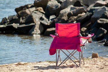 Close up, isolated image of a foldable fabric camping chair with metal legs placed on the sand at...
