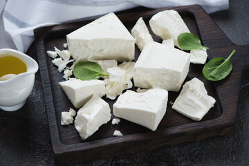 Closeup of a black wooden serving board with chunks of feta cheese, selective focus, studio shot
