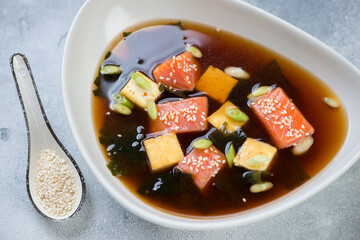 Miso soup with chunks of salmon fillet, tofu cheese, wakame and green onion served in a grey bowl, studio shot
