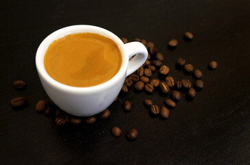 Espresso coffee in a white mug and coffee beans on the table.