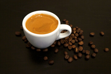 Espresso coffee in a white mug and coffee beans on the table.